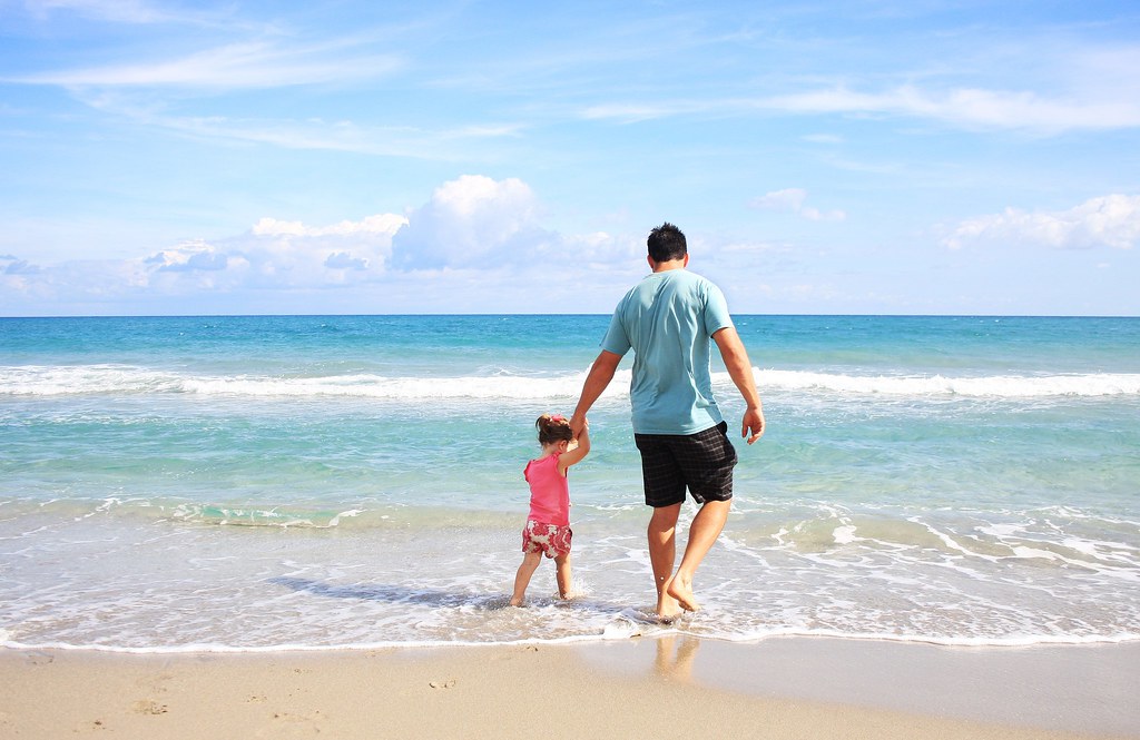 photograph of father walking with daughter in the water on the beach