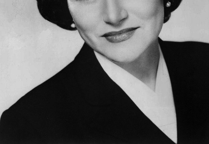 Cropped, black-and-white headshot of a white woman with dark hair, pearl earrings wearing a white blouse and dark blazer.