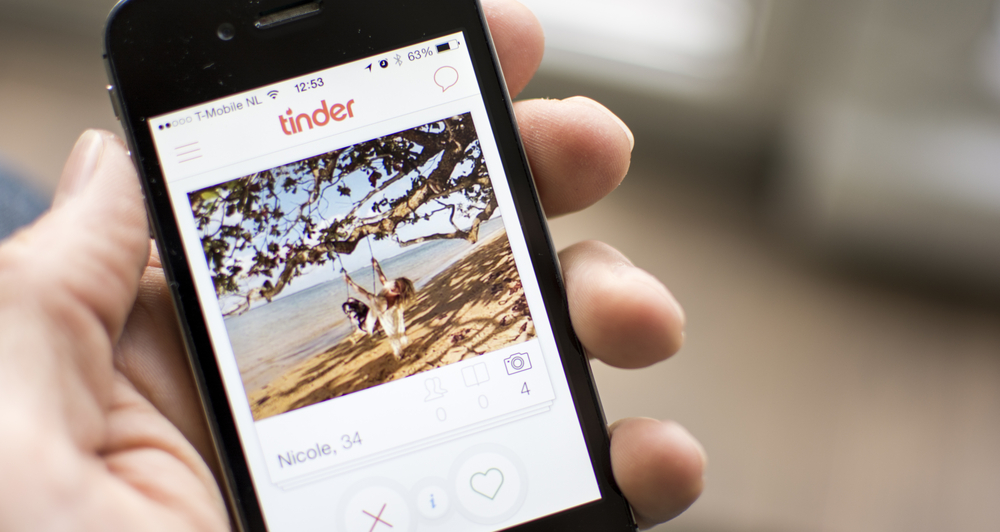 photograph of person looking at phone display of tinder profile