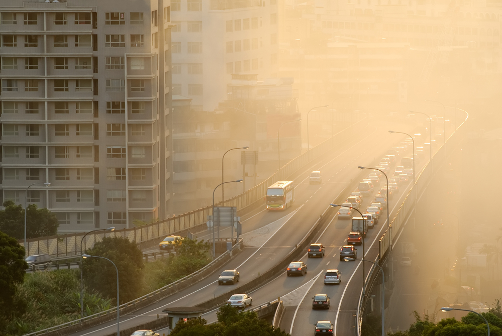photograph of air pollution with cars on highway and yellow smoke in city