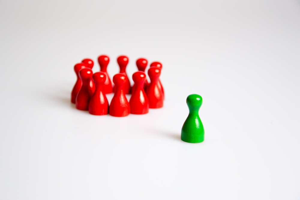 photograph of green board game piece isolated from huddled, red board game pieces