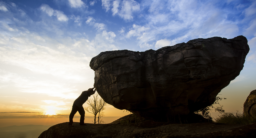 photograph of silhoutted man leaning against boulder at dawn