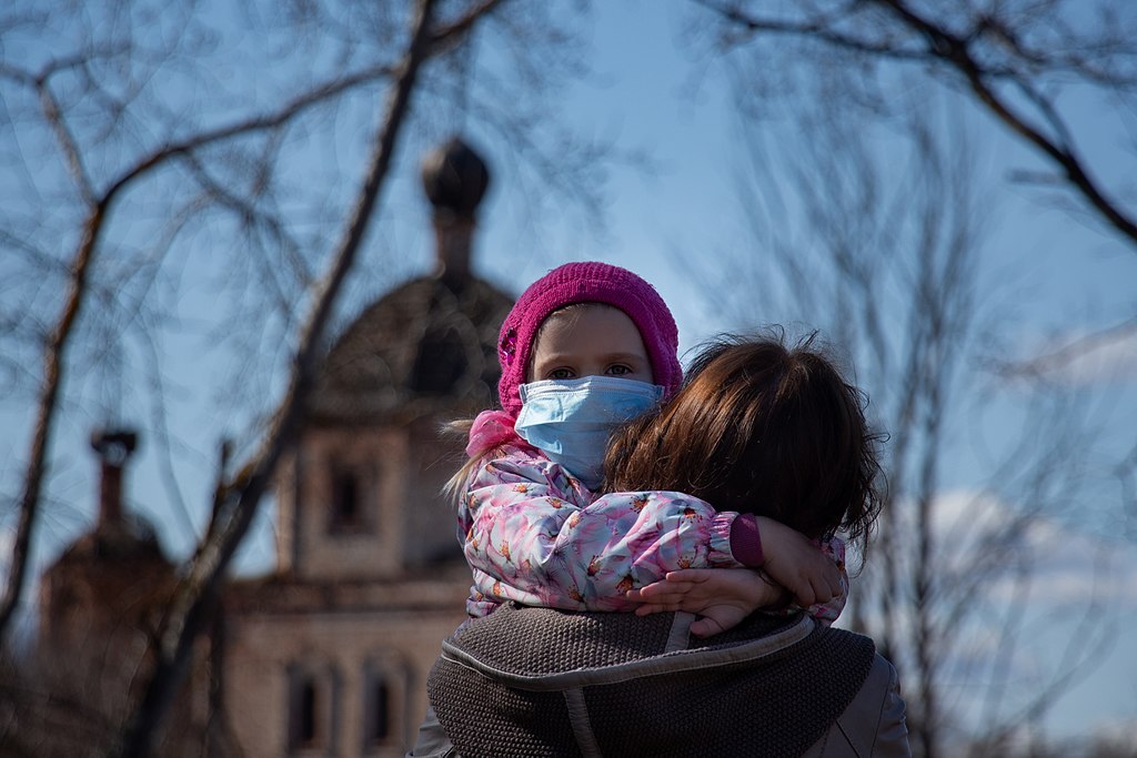 photograph of child with mask hugging her mother