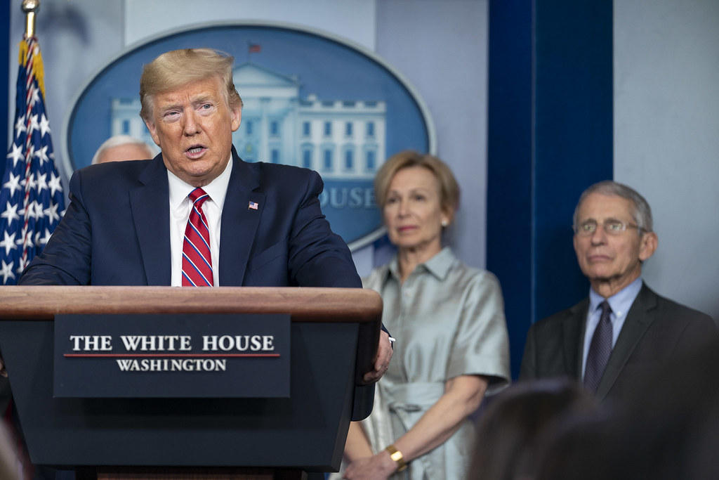 photograph of Trump at podium with Dr. Fauci and Dr. Bix behind him.