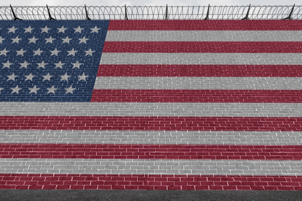 photograph of American flag painted on side of brick wall with barb wire strung on top