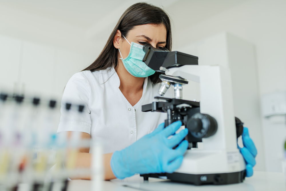 photograph of scientist with mask and gloves looking through microscope