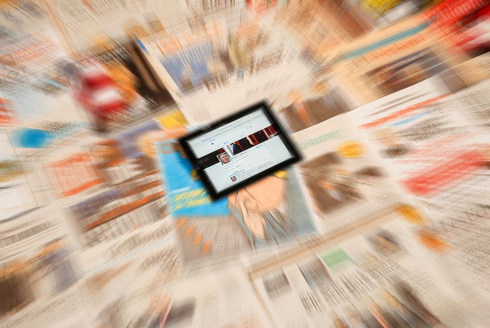 photograph of ipad with Trump's twitter profile sitting atop various blurred newspaper front pages feating him