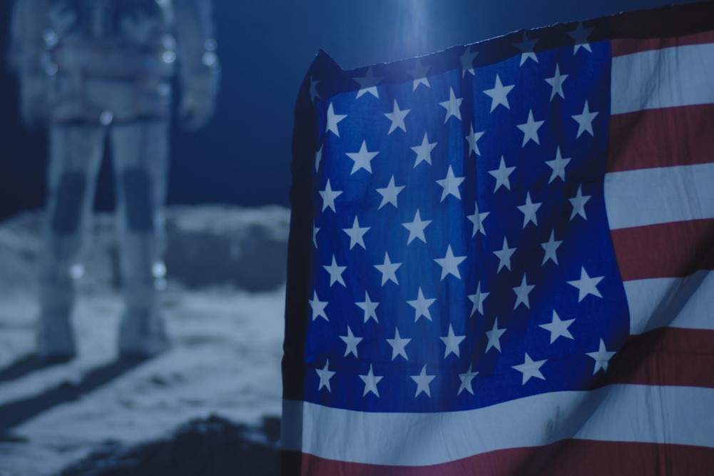 photograph of American flag planted on Moon with Astronaut staring off into space
