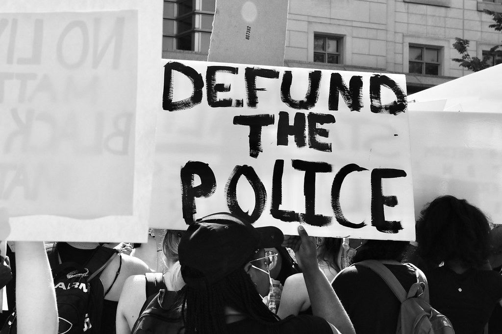 black-and-white photgraph of protestors holding "Defund the Police" sign