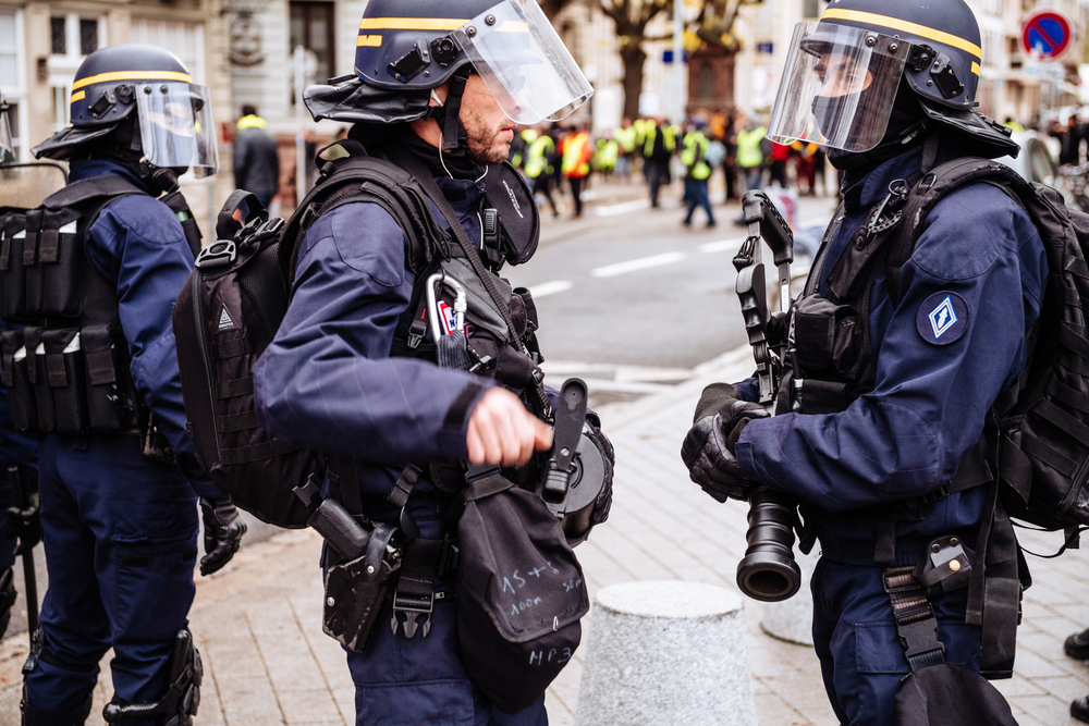 two police officers dressed in riot gear holding smoke grenade guns
