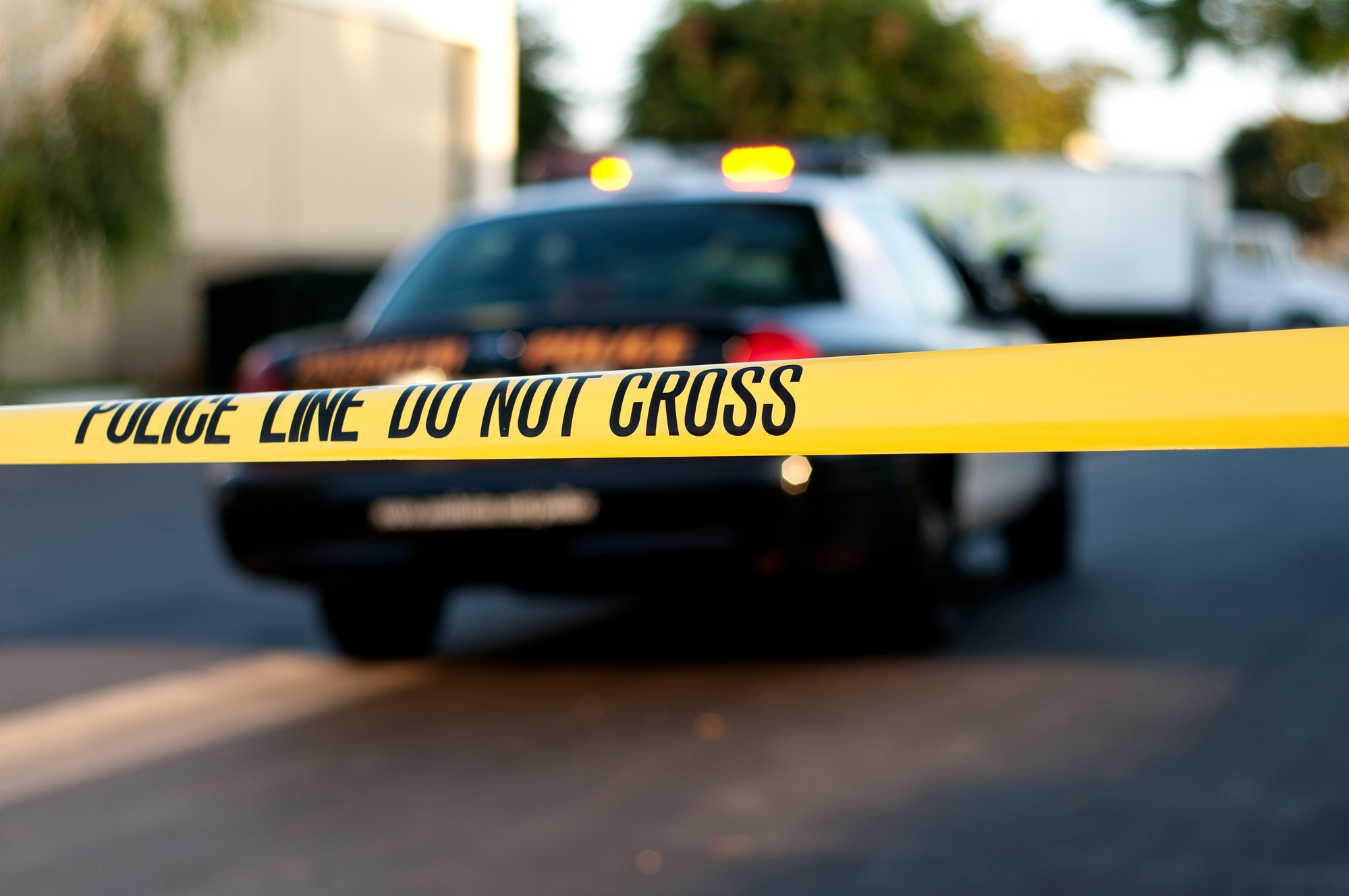 photograph of crime scene tape with police car in background