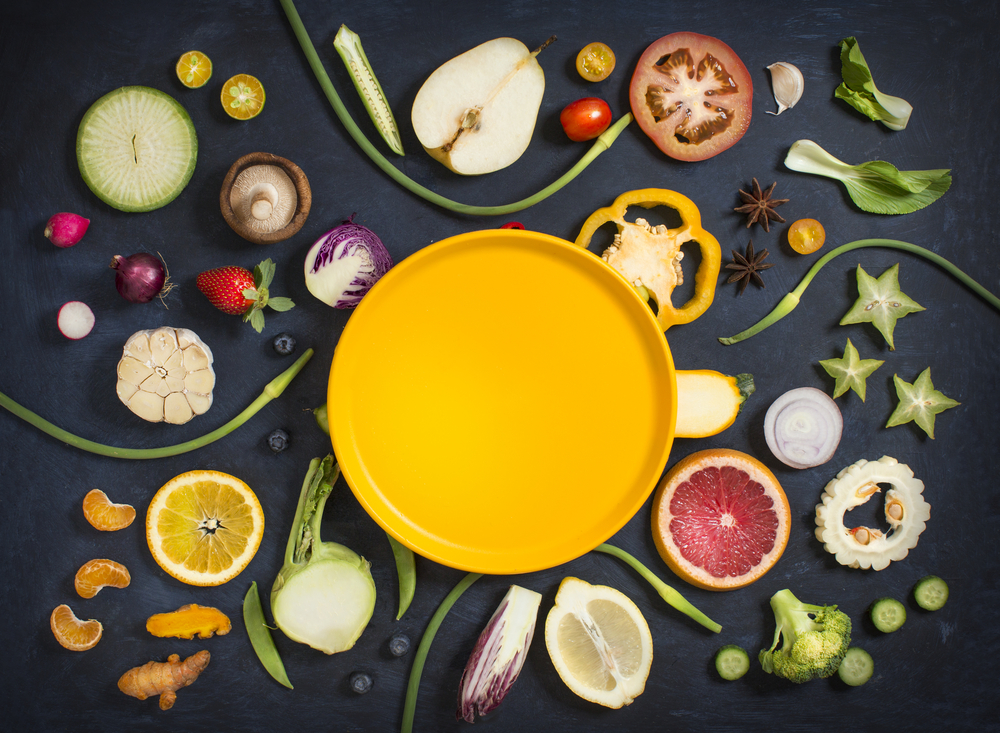 photograph of halved fruits and vegetables arranged around yellow plate in the center