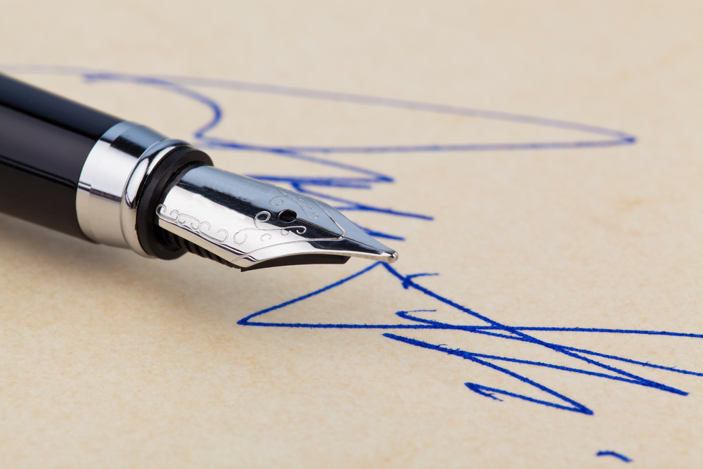 photograph of a fountain pen and a signature on yellow paper.