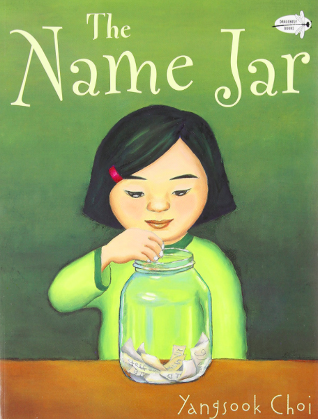 Cover image for The Name Jar with an illustration of a young Korean girl with a bob and a red barrette wearing a bright green shirt. She has a large glass jar on a table in front of her. It is filled with small slips of paper, and she is reaching in the lip of the jar to get one.