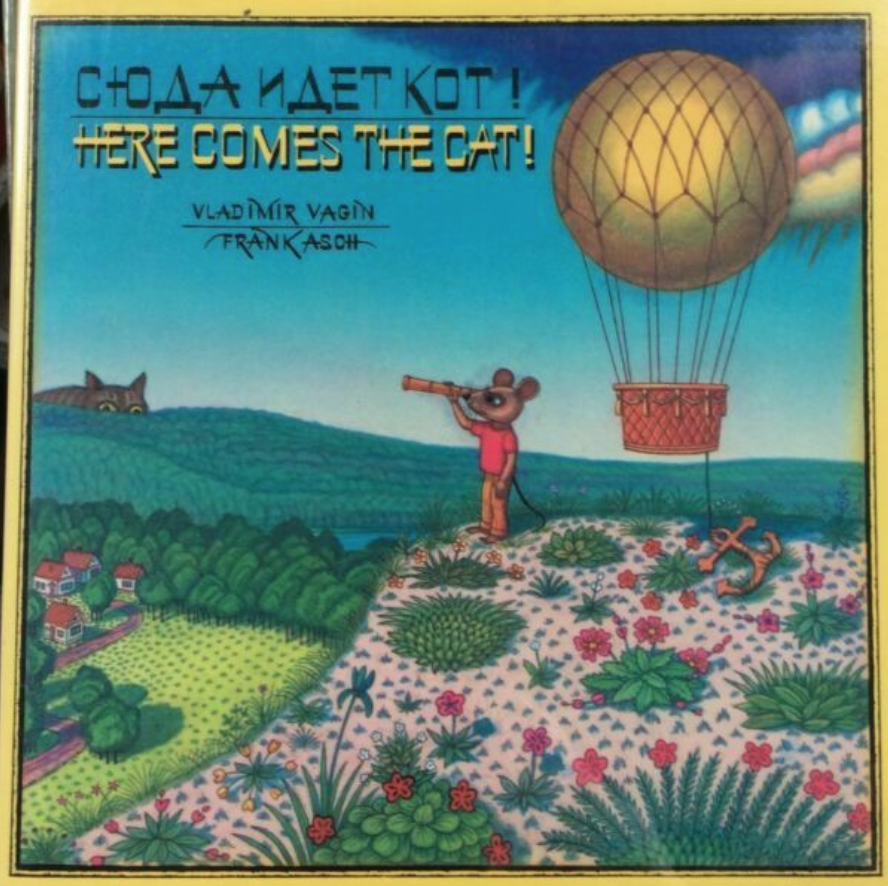 Illustrated book cover for Here Comes the Cat featuring a mouse looking through a spyglass at a cat. The mouse stands atop a hill with a hot air balloon nearby. The cat peeks over the hills past the village.