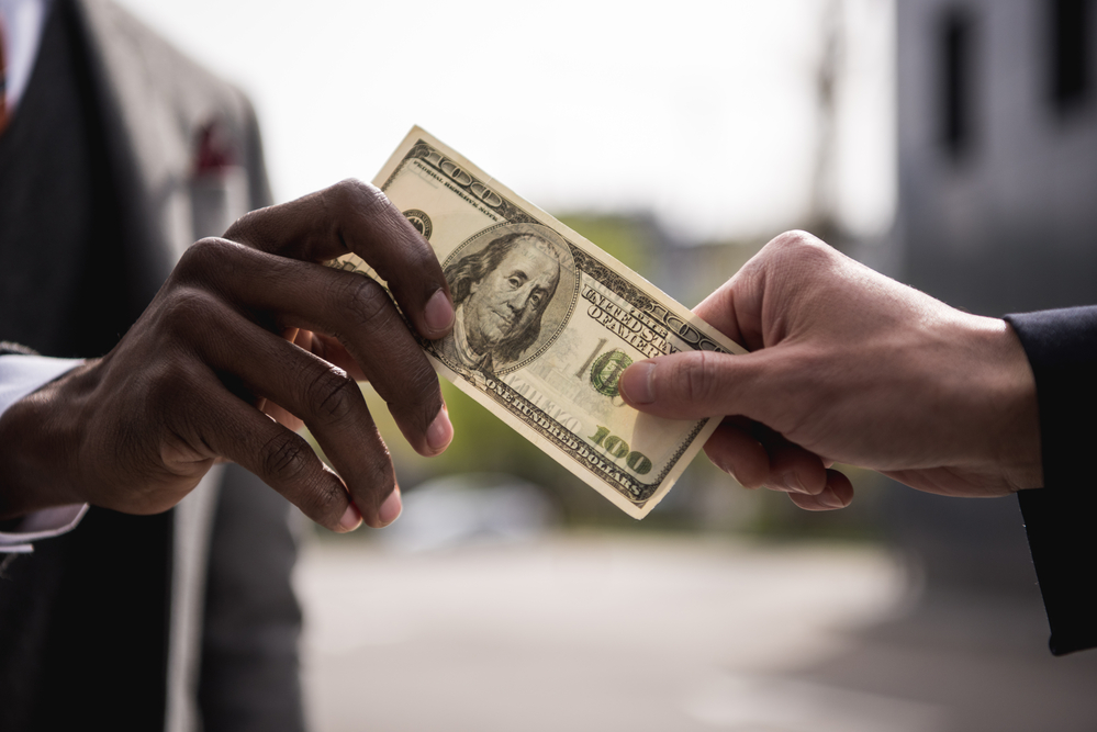 photograph of hands exchanging a one hundred dollar banknote