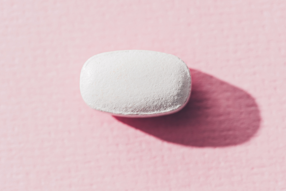 close-up photograph of white, chalky pill on pink background