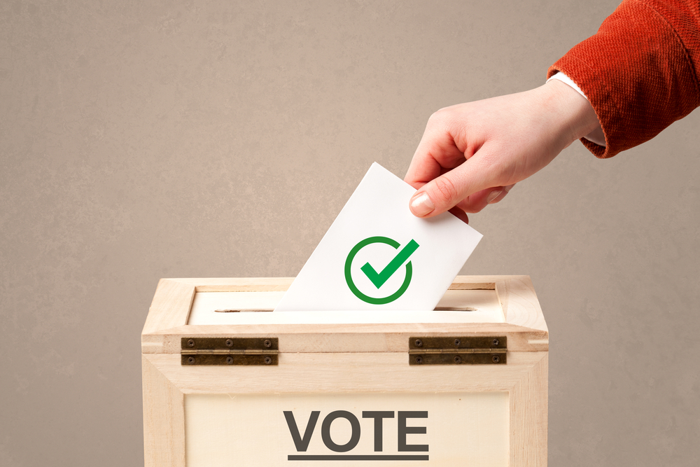 close up photograph of male hand putting vote into a ballot box