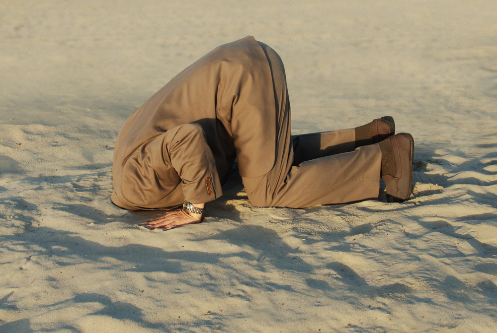 photograph of business man with his head buried in the sand