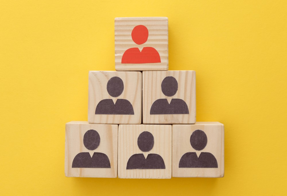 photograph of pyramid of wooden cubes indicating people on yellow background