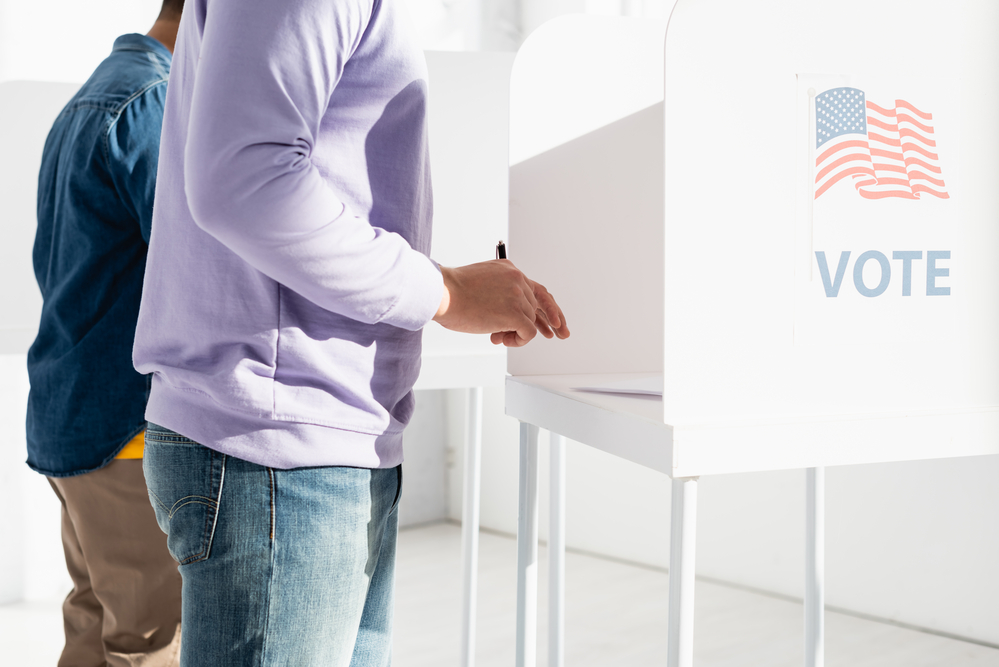 photograph of citizens filling out voting ballots with "Vote" sticker on booth