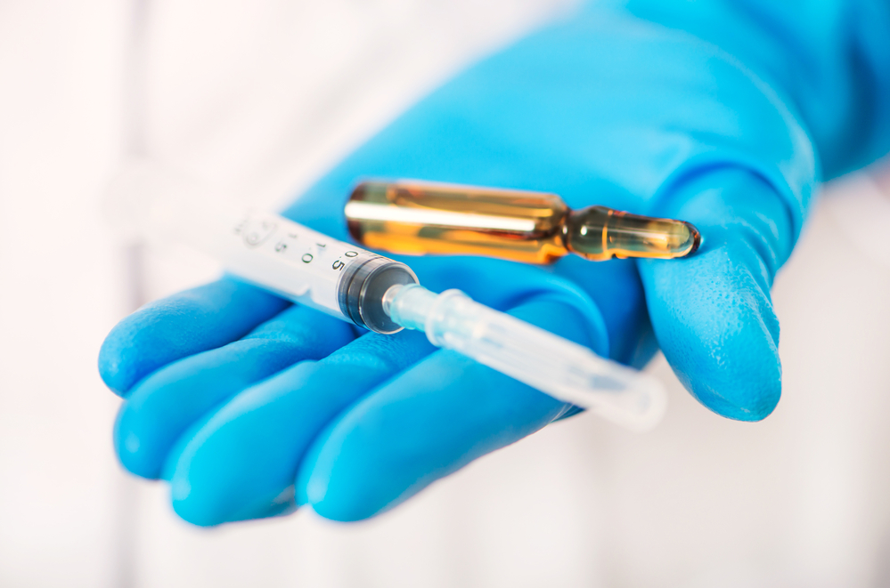 photograph of gloved hand offering syringe and vaccine vial