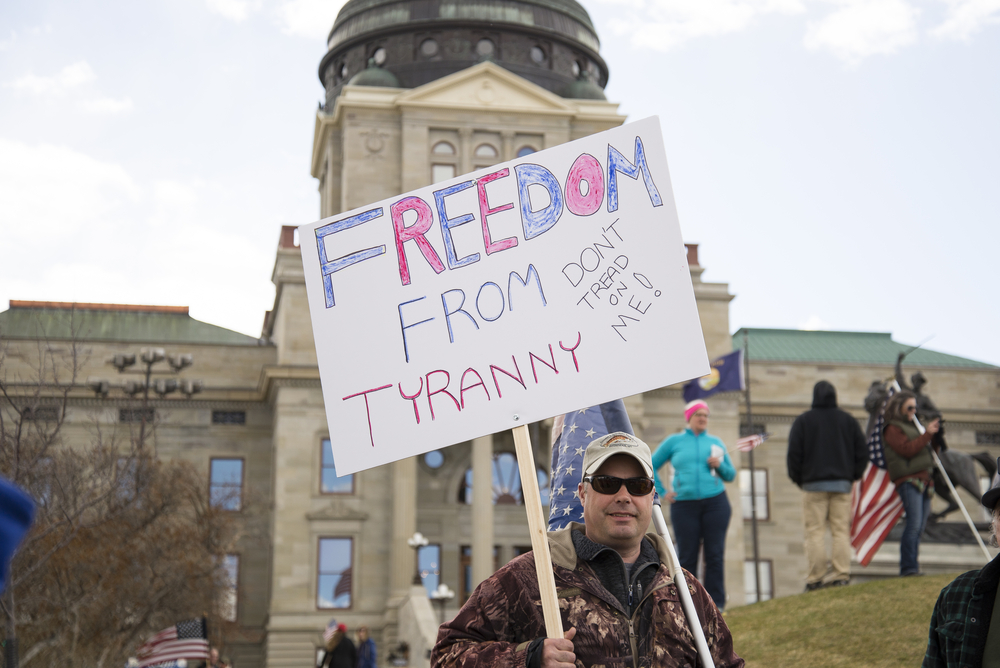 photograph of protester holding sign reading: "Freedom from Tyranny Don't Tread on Me" in front of State building