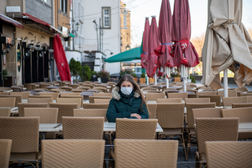 photograph of woman with face mask sitting in large, empty street dining area
