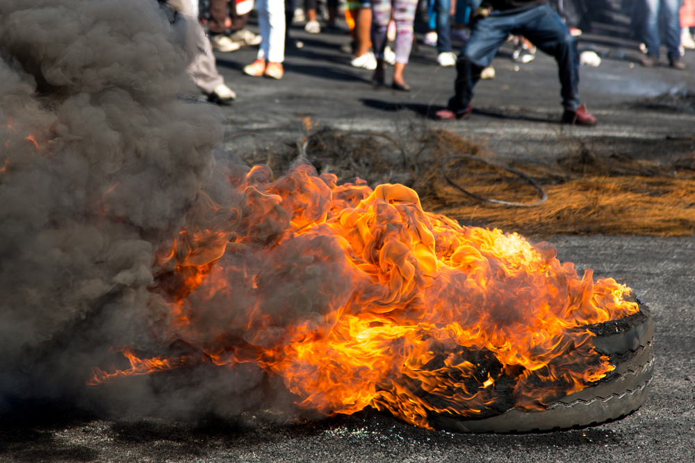 photograph of a burning tire with the feet of a crowd of protestors in the background