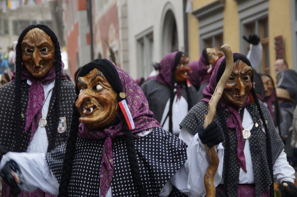 photograph of a crowd marching the streets dressed as witches and wearing grotesque masks