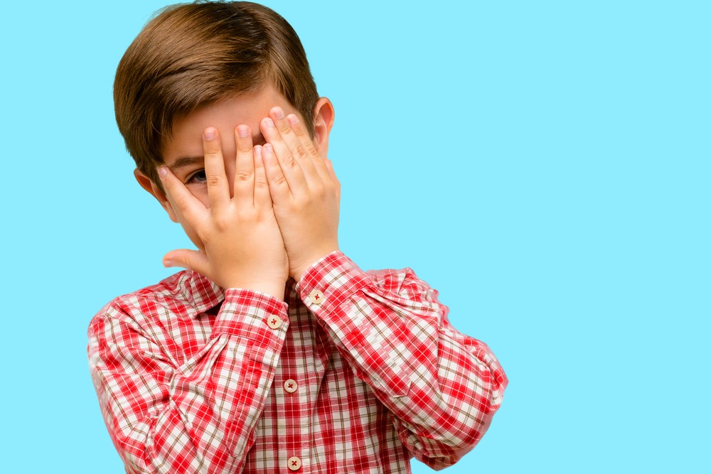 photograph of small child peeking through his hands covering his face