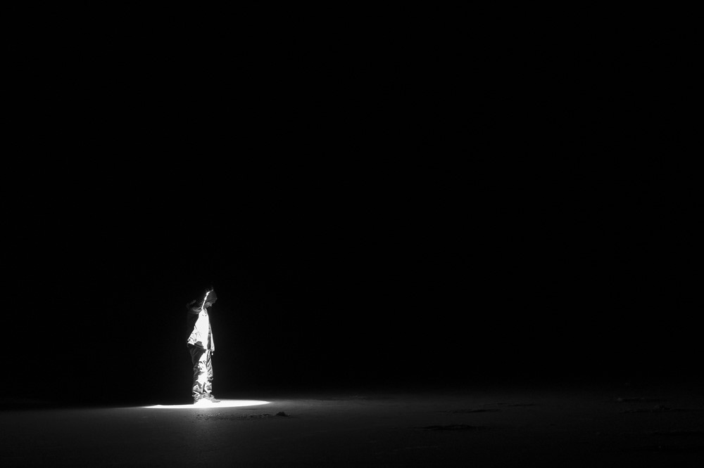 photograph of single person with flashlight standing in pitch darkness