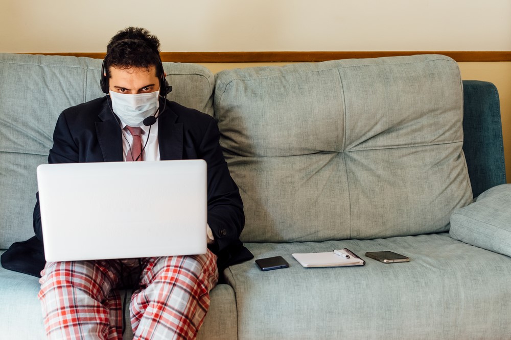photograph of masked businessmen in tie and pajamas working at laptop at home