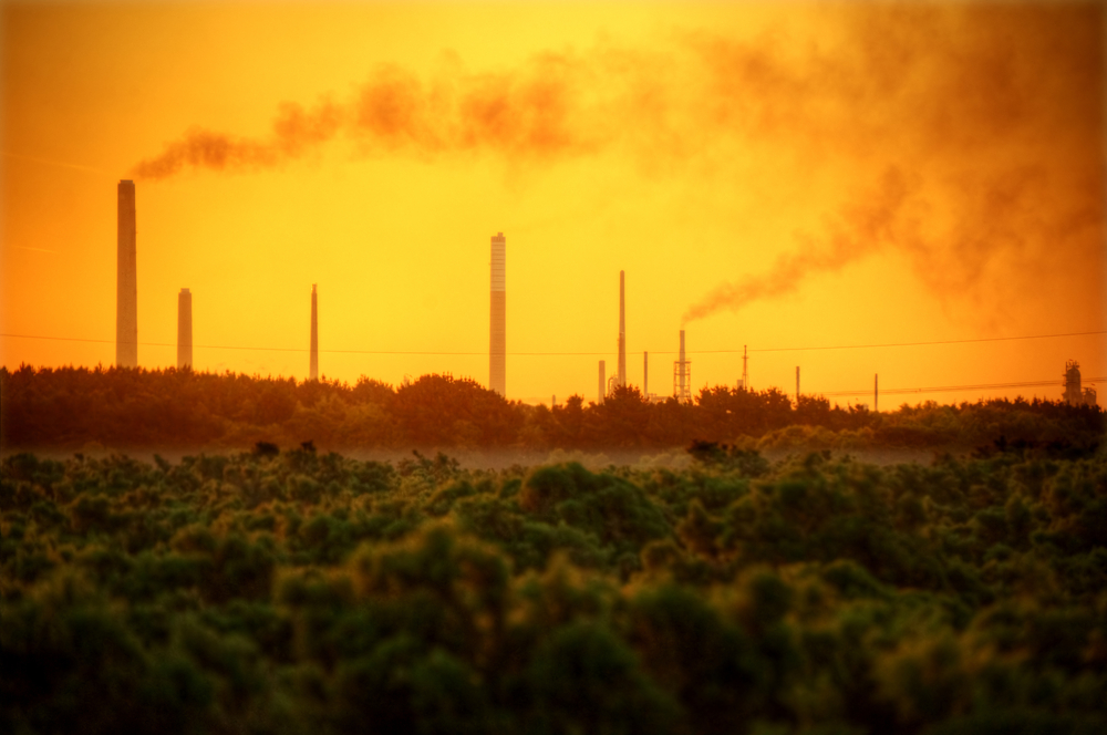 photograph of industrial chimney stacks polluting air over natural landscape