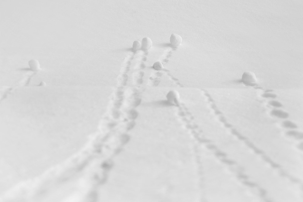photograph of several snowballs at the bottom of hill with tracks trailing behind