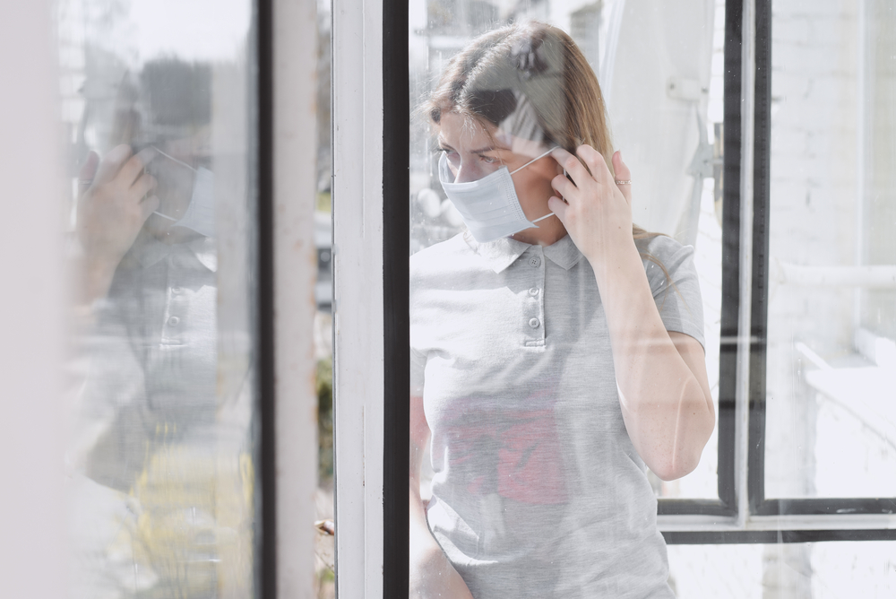 photograph of woman in masking looking at reflection in the window