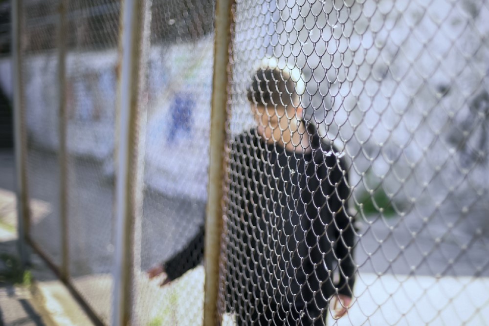 photograph of teen boy confined behind chain link fence