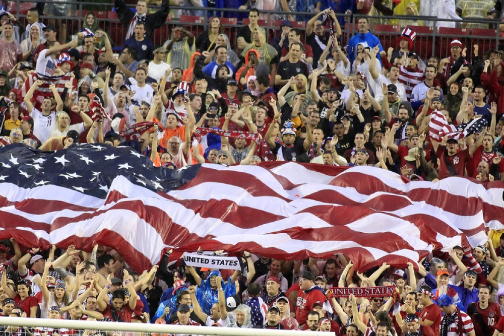 photograph of fans in crowded stadium holding one big American flag