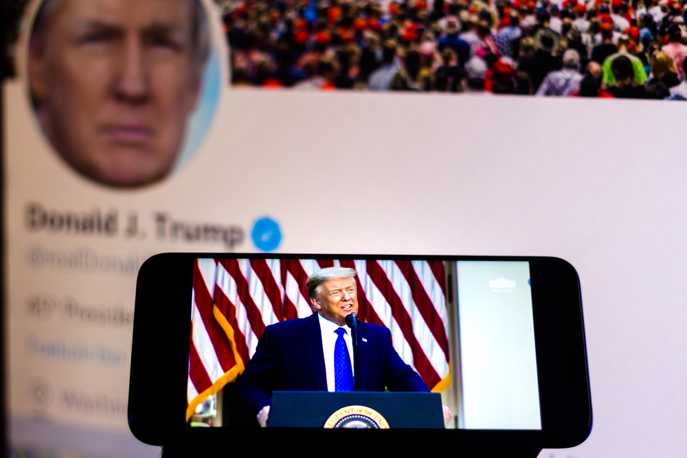 photograph of trump speech playing on phone with Trump's Twitter page displayed in the background