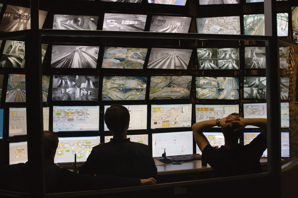 photograph of silhouettes watching surveillance monitors