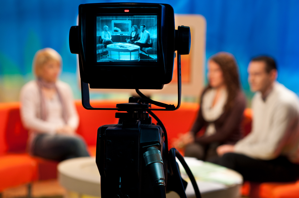 photograph of TV studio with actors displayed in camera viewfinder