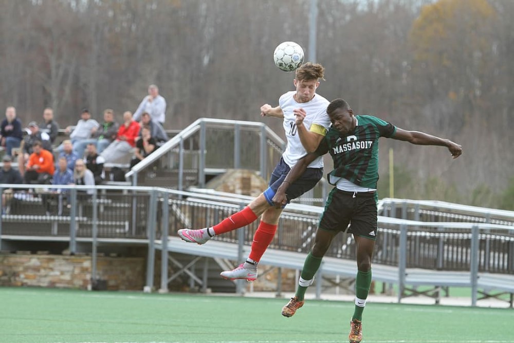 photograph of two soccer players competing in air for ball