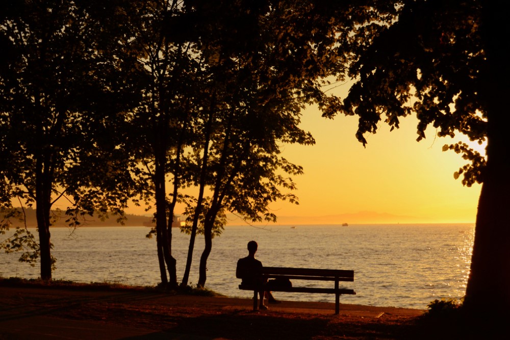 photograph of silhouetted figure alone on bench at sunset