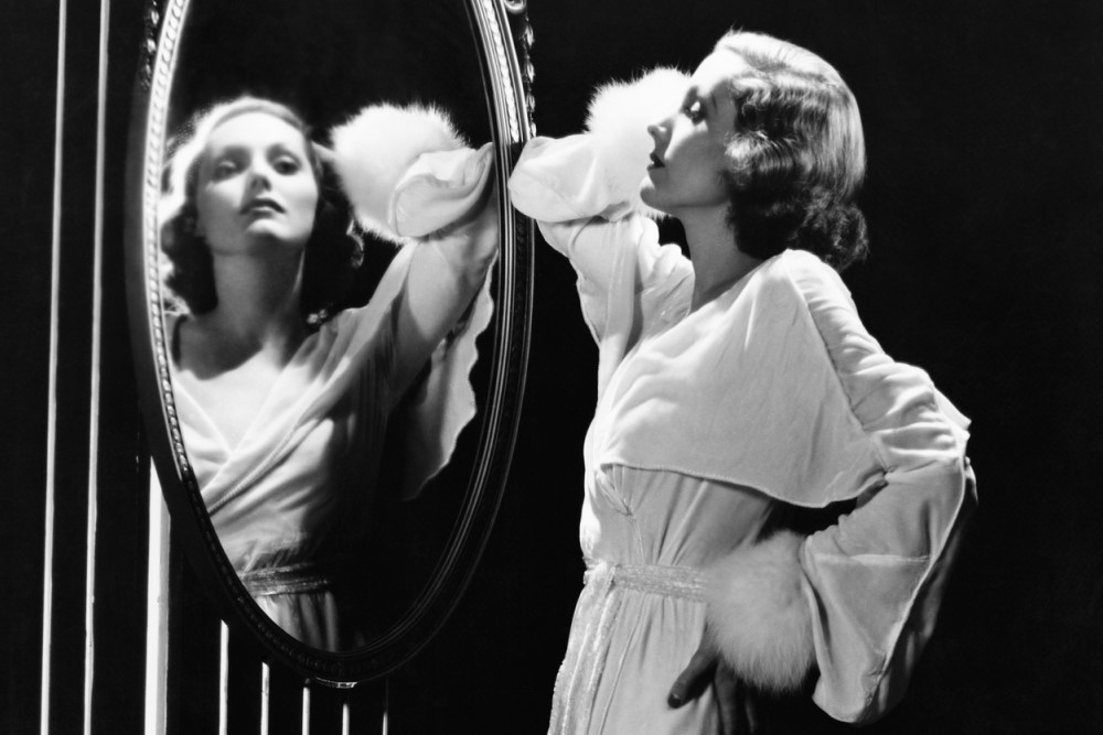 black-and-white photograph of glamorous woman looking in mirror