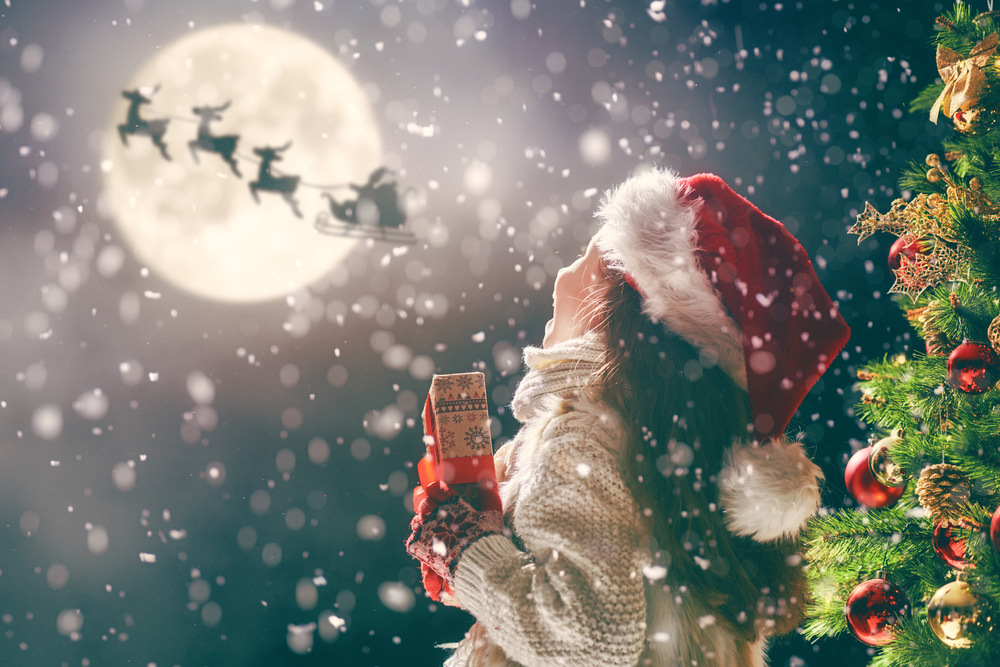 photograph of child with present watching silhoette of Santa's sleigh