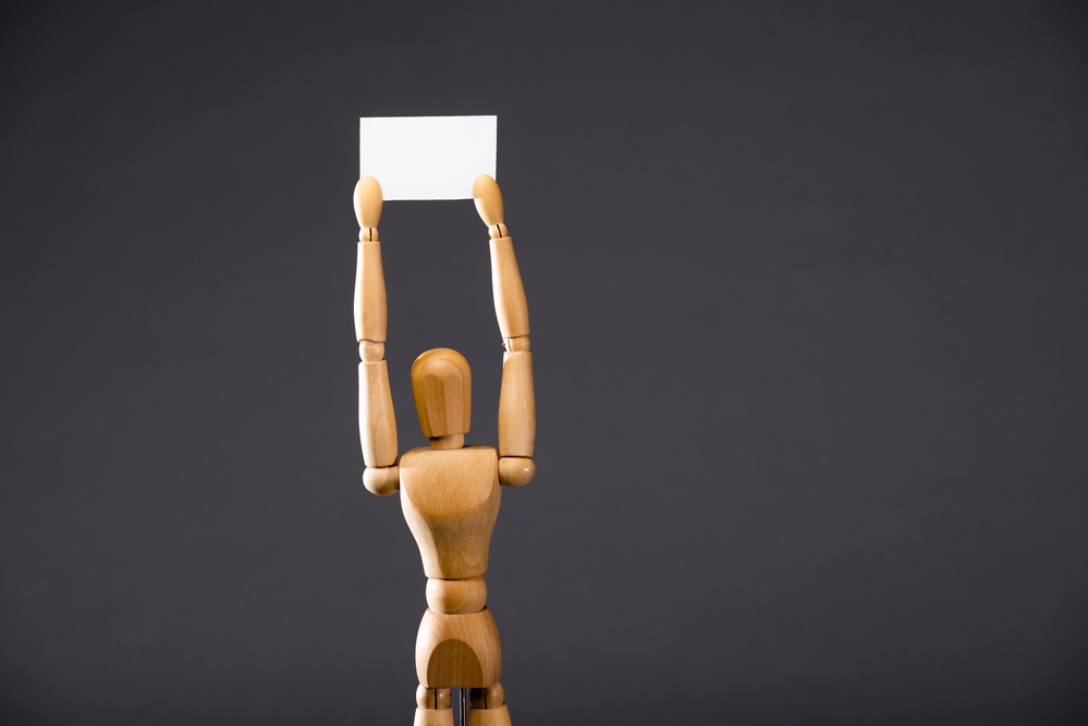 photograph of lone wooden figurine holding sign