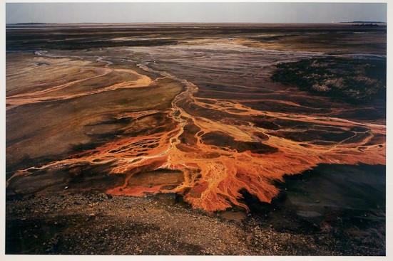 Nickel Tailings 30 Sudbury Ontario by Edward Burtynsky is a saturated color photograph of copper-colored chemical runoff. The land is covered in the runoff, and looks like rivers of bright orange liquid.
