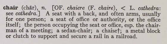 Close-up photograph of the dictionary text from the gallery installation of Joseph Kosuth's "One and Three Chairs." It reads: "A seat with a back, and often arms, usually for one person; a seat of office or authority, or the office itself; the person occupying the seat or office, esp. the chairman of the meeting; a sedan-chair; a chaise; a metal block or clutch to support and secure a rail in a railroad."