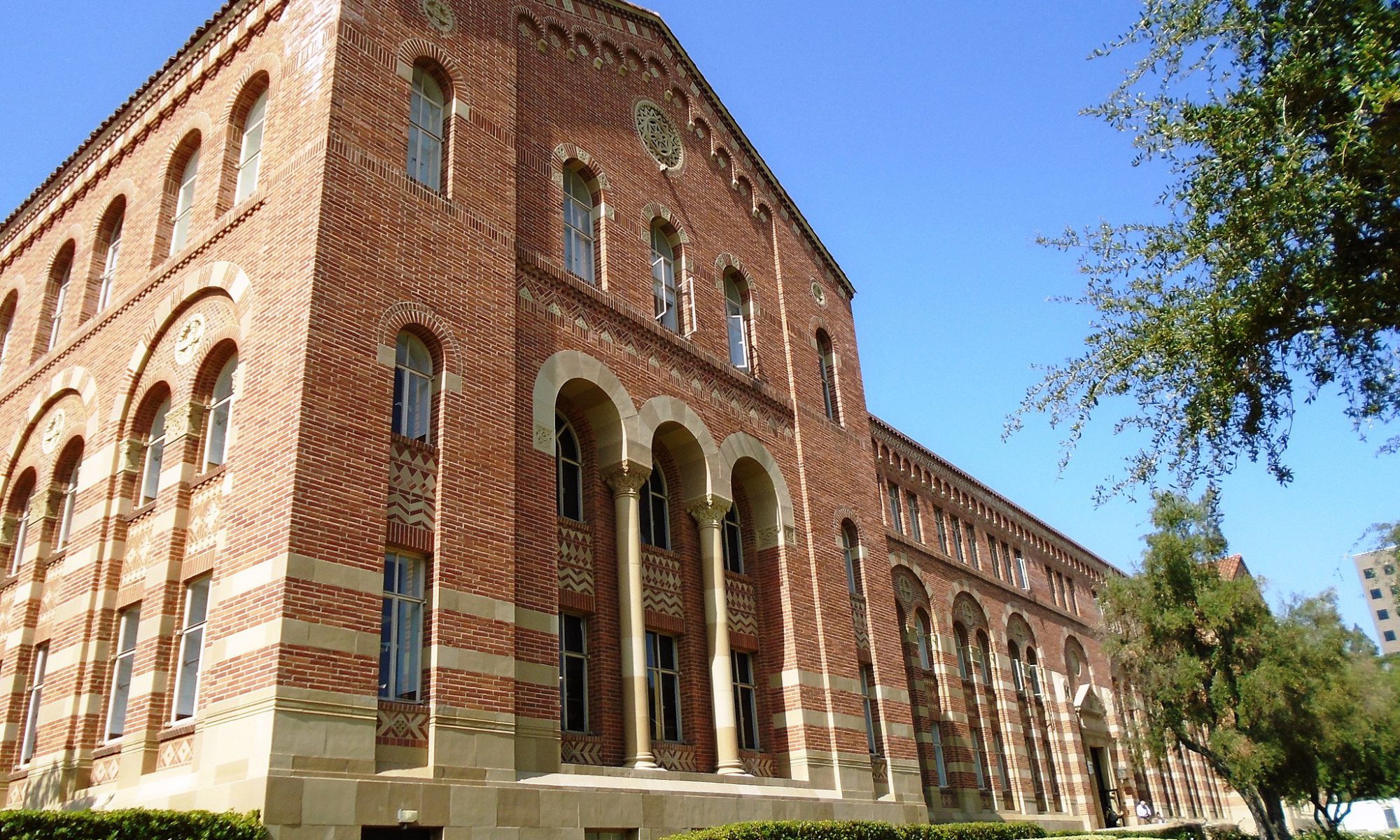 Color photograph of Haines Hall at UCLA, a large red brick building with lots of Romanesque arches