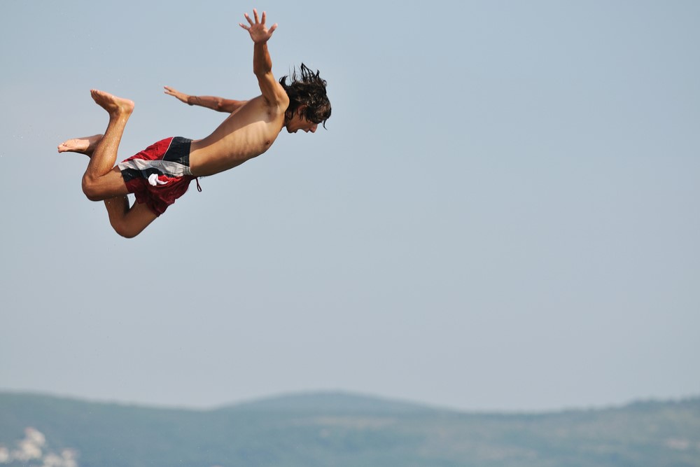 photograph of boy cliff-jumping into sea